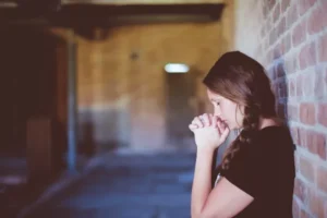 woman praying leaning against wall